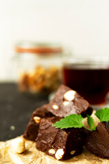 Fondant on craft crumpled paper with nuts and chocolate cubes decorated with green mint leaves. In the background a jar of nuts, blurred background. Sweet composition on a black textural background. 