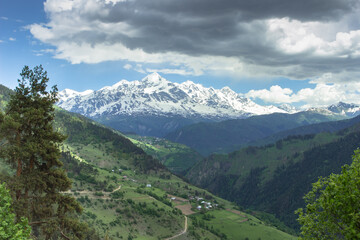 Fototapeta na wymiar Amazing view of the mountains, wild nature and green valley. Trekking in the mountains. Rural village with farmhouses. View of the countryside. High peaks of the Great Caucasus with snow