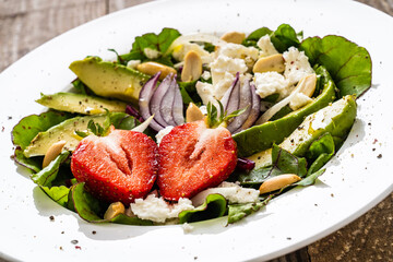 Fresh salad - feta cheese, avocado, lettuce, strawberries and onion on wooden table