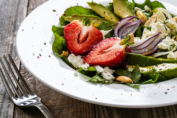 Fresh salad - feta cheese, avocado, lettuce, strawberries and onion on wooden table