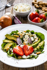 Fresh salad - feta cheese, avocado, lettuce, strawberries and onion on wooden table