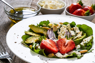 Fresh salad - feta cheese, avocado, lettuce, strawberries and onion on wooden table