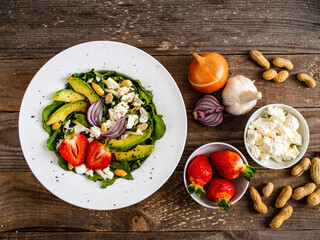 Fresh salad - feta cheese, avocado, lettuce, strawberries and onion on wooden table