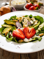 Fresh salad - feta cheese, avocado, lettuce, strawberries and onion on wooden table