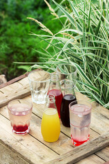 Strawberry, cherry and rhubarb syrups and glasses with water on a wooden table in the garden.