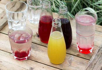 Strawberry, cherry and rhubarb syrups and glasses with water on a wooden table in the garden.