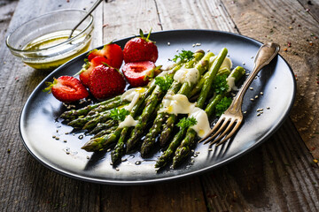Tasty breakfast. Green asparagus with mozzarella and strawberries served on black plate on wooden table
