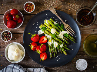 Tasty breakfast. Green asparagus with mozzarella and strawberries served on black plate on wooden table
