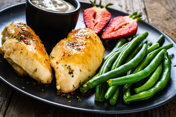 Roast chicken fillets with green beans and strawberries on wooden table

