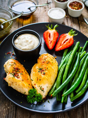 Roasted chicken fillets with green beans and strawberries on wooden table
