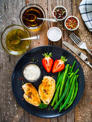 Roasted chicken fillets with green beans and strawberries on wooden table
