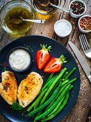 Roasted chicken fillets with green beans and strawberries on wooden table
