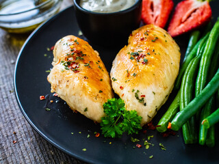 Roasted chicken fillets with green beans and strawberries on wooden table
