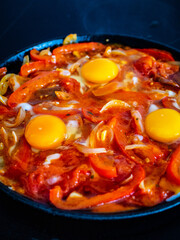 Shakshuka - fried eggs with chorizo and vegetables in frying pan
