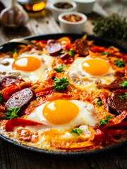Shakshuka - fried eggs with chorizo and vegetables in frying pan
