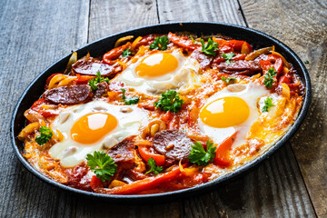 Shakshuka - fried eggs with chorizo and vegetables in frying pan
