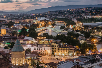 Beautiful panoramic view of evening Tbilisi, capital of Georgia. City colorful lights, river,cathedral,old buildings at a nice sunset mountains in the background.Evening city scene