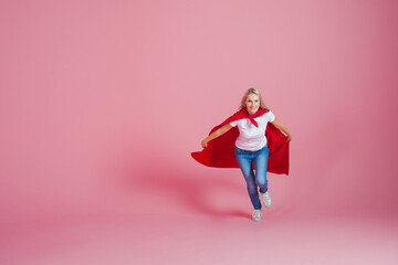 running superhero. Funny young woman in the image of a superhero to the rescue. Pink background