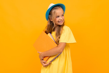 Beautiful girl with long hair holds a notebook and smiles, picture isolated on yellow background