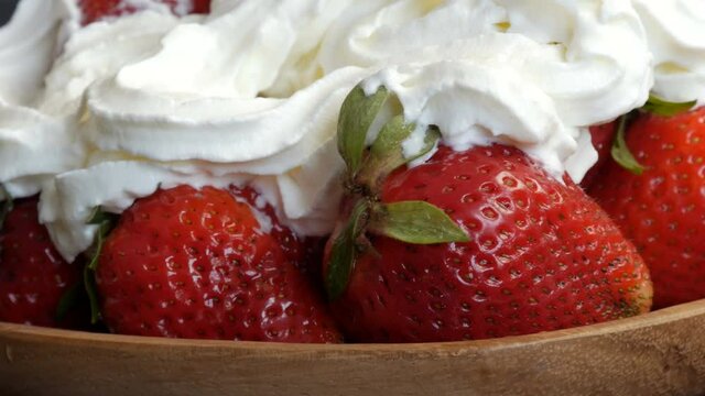 Juicy ripe big red strawberries on an eco bamboo plate on top with whipped cream cloes up view.