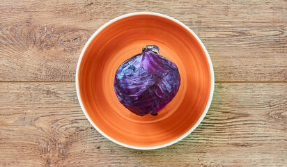 purple head of red cabbage on a orange plate on a wooden tabletop