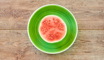 small ripe halved watermelon on a green plate on a wooden tabletop