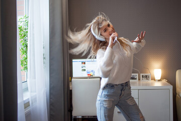 cheerful girl with a phone and big headphones is dancing and singing. Holds the phone as a...