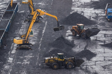 EXCAVATORS AND WHEEL LOADER - Machines at reloading work on a coal yard in rainy weather