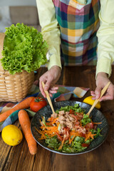 Making salad with tuna, lettuce, carrot, tomato, arugula, cucumber, olive oil, lemon.