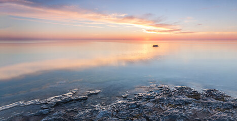 Sunrise over the sea horizon. The calm Baltic Sea is colored in blue, orange and yellow. The island of Gotland, Sweden.	