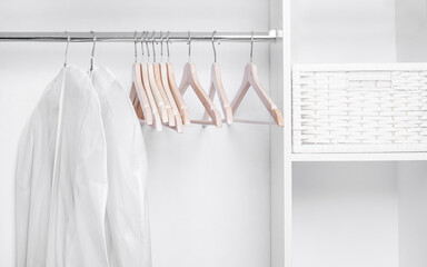 Wooden hangers and covers for clothes in a white minimalistic wardrobe.