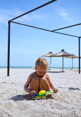 Small cute baby boy busy playing with concrete mixer toy plastic car, fill with sand by scoop, happy vacation at sea beach 