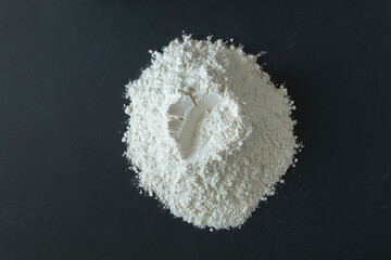 Close-up of white wheat flour on a black surface. Horizontal orientation, top view.