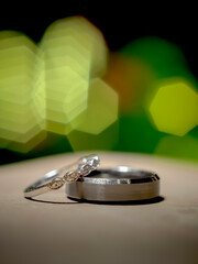 a pair of rings posed one on top of the other in an elegant silver color, with embedded stones on a defocused surface and with a background of green lights out of focus
