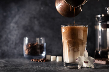 Popular cold coffee with ice and milk in a transparent glass, on a dark background. The concept of refreshing and invigorating drinks in the summer heat. selective focus.
