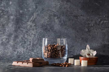 coffee beans in a glass Cup, an Orchid flower, sugar cubes and chocolate on a dark graphite background. selective focus.