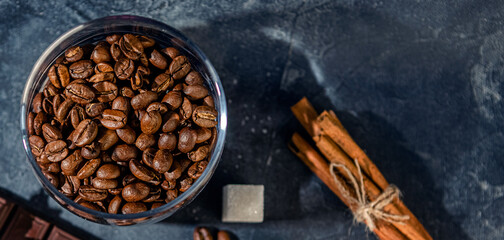coffee beans in a glass Cup, cinnamon sticks and chocolate on a dark graphite background. selective...
