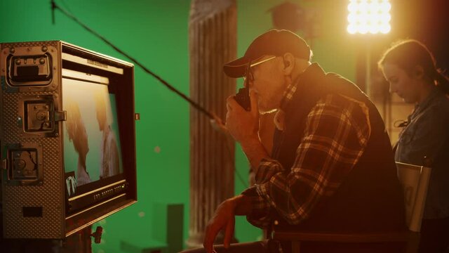 Director Looks at Display Controls Shooting Period Drama Movie. Green Screen CGI Scene with Actors Wearing Renaissance Costumes. Big Film Studio Professional Crew Shooting High Budget Movie. Side View