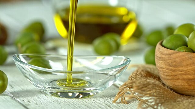 Super Slow Motion Shot of Pouring Fresh Olive Oil into Glass Bowl on White Wooden Table at 1000 fps.