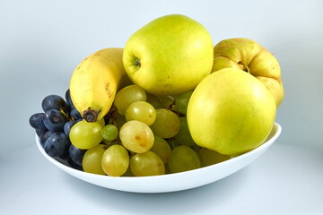 Two apples, a banana, a quince, white grapes, black grapes on a white plate