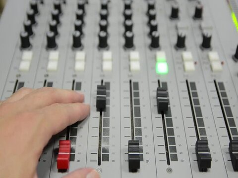 Hand on a mixer. Close up of professional multitrack mixing console in the control room. Technician in Radio station. Equipment in studio. Recording and broadcasting program. Live show. On air.