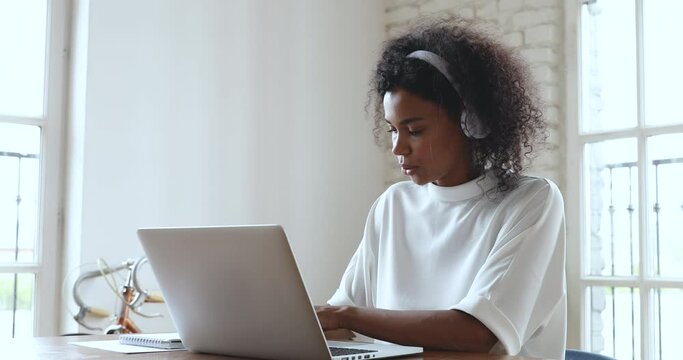 Happy african business woman teacher student operator wear wireless headphone make video conference call in office typing talk by webcam on laptop, distance education elearning online study concept