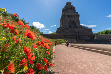 The Monument to the Battle of the Nations at blue sky and red poppy flowers