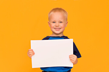 Happy boy with a smile holds a blank white sheet. Yellow background copy space