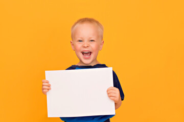 Happy boy with a smile holds a blank white sheet. Yellow background copy space