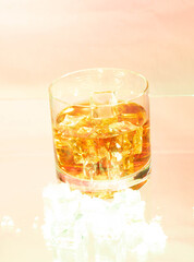 appetizing glass of whiskey on the glass table next to cold ice in a medium quality pink light setting