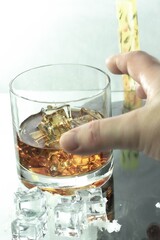 fingers reaching for glass of appetizing whiskey on glass table next to cold ice