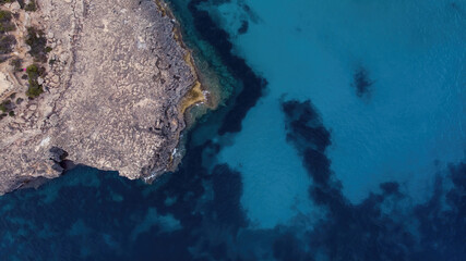 Aerial view of the rocky coast on a calm electric blue sea