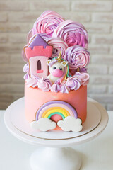 Cute pink birthday cake for a little girl with fondant unicorn, gingerbread princess castle, rainbow and meringue.