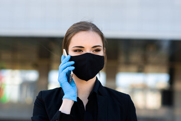 Beautiful businesswoman in a black suit in a black medical mask and gloves at the city in quarantine and isolation. Pandemic COVID-19. Selective focus